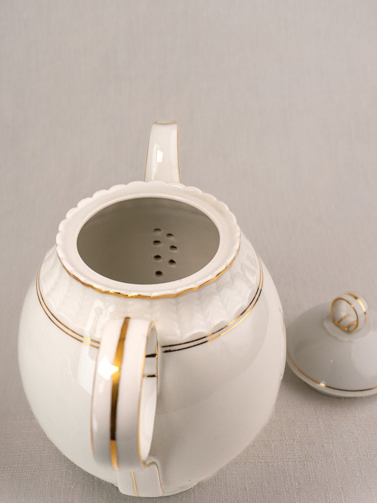 Antique Bernardaud Limoges porcelain teapot with gold accents, lid beside on light surface.