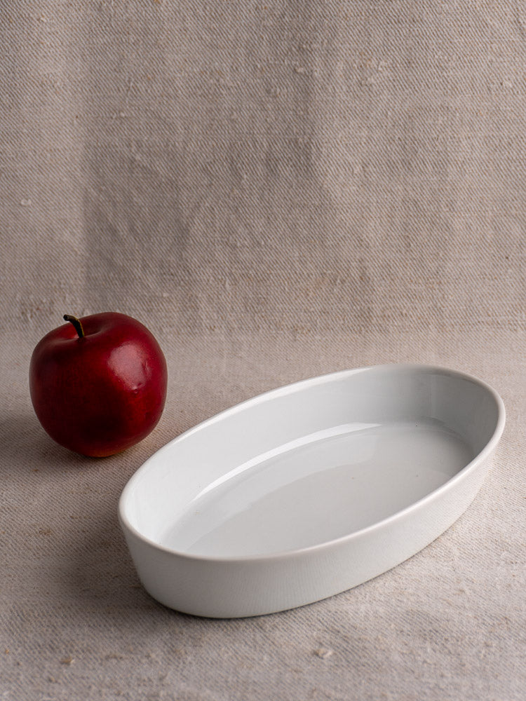 Vintage French CNP white porcelain oval serving dish on a textured beige fabric surface.