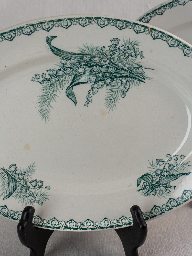 Antique French Saint Amand faience platter with green botanical border, displayed on black stand.