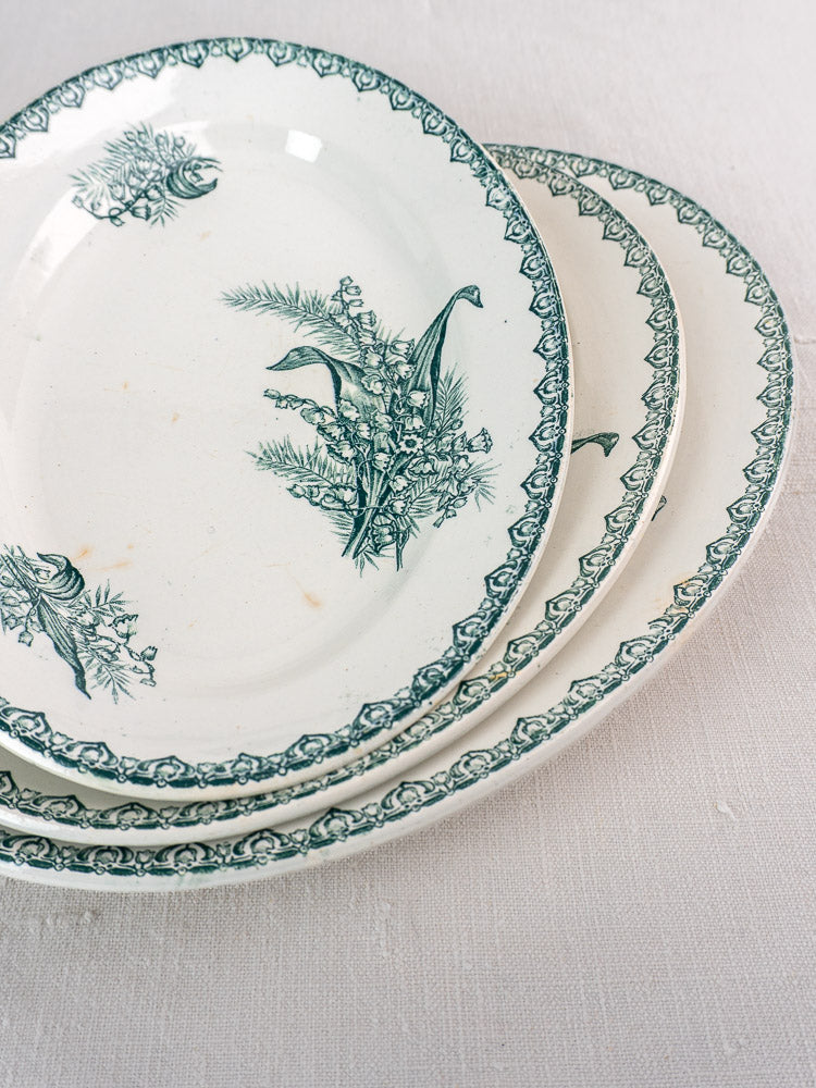 Set of five antique French Saint Amand Muguet faience platters with green floral patterns on white.