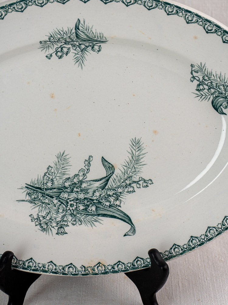 Antique French Saint Amand Muguet faience platter with green floral motifs, vintage wear, on black stand.