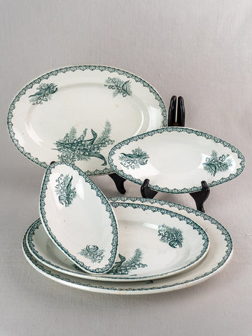 Set of five antique French Saint Amand faience platters with green Muguet floral motifs, upright on gray background.