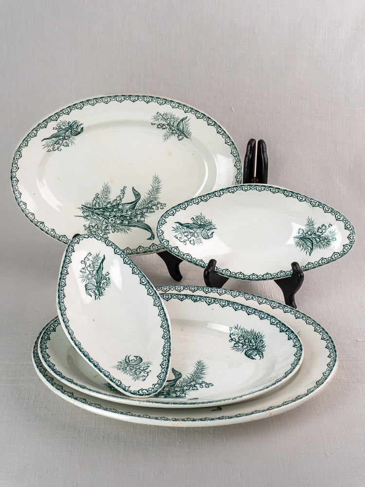 Set of five antique French Saint Amand faience platters with green Muguet floral motifs, upright on gray background.