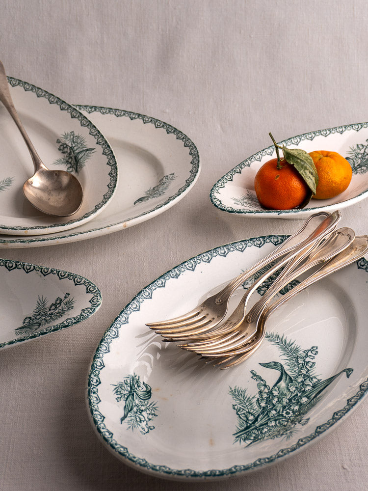 Antique French Saint Amand Muguet five-piece faience platter set with green floral motif, silverware, and oranges on light fabric.