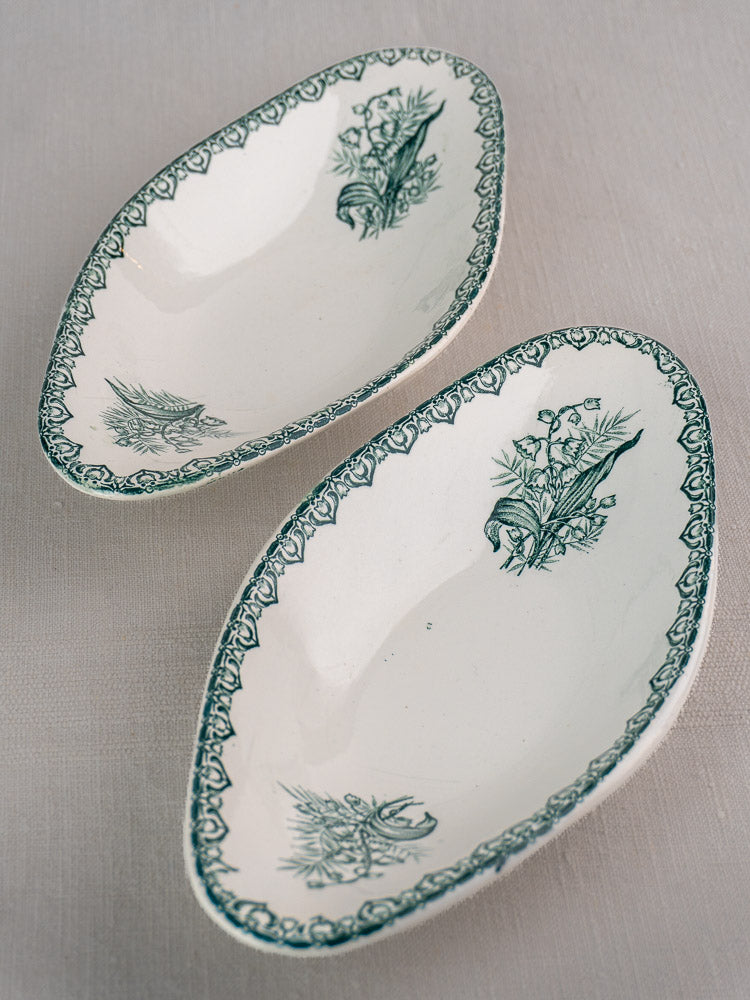 Set of five antique French Saint Amand Muguet faience platters with green floral accents, on light fabric.
