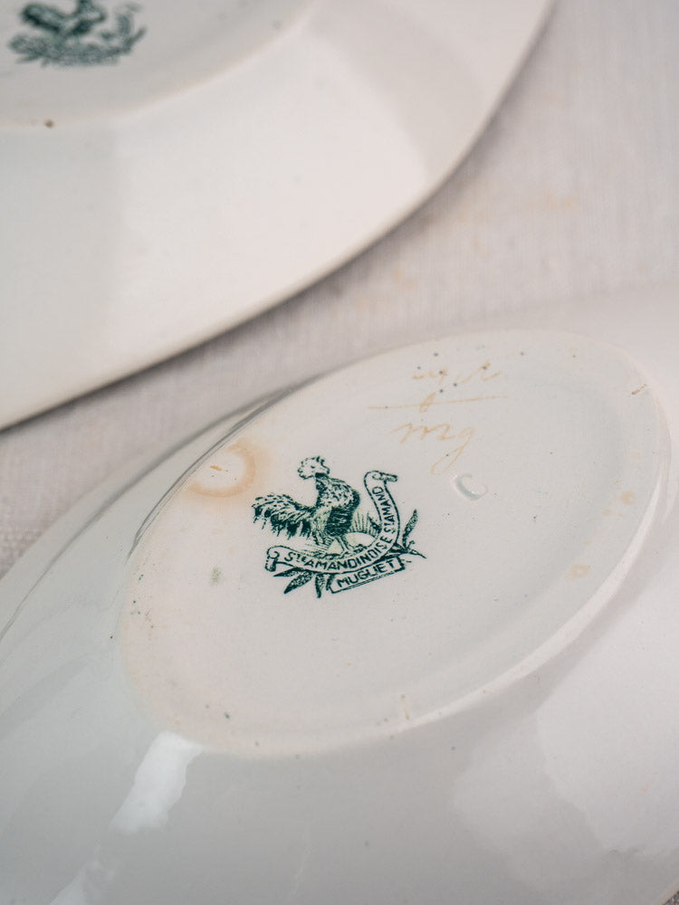 Antique French Saint Amand Muguet faience platter underside with green bird maker’s mark; another platter behind.