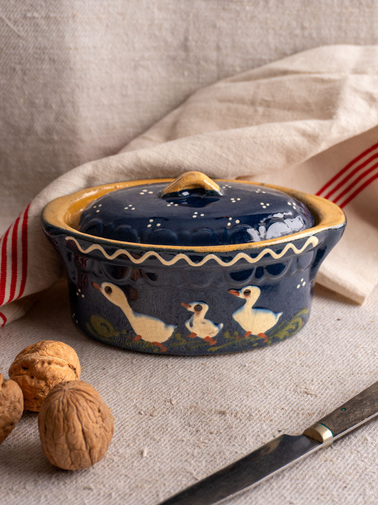 Antique French Soufflenheim covered terrine in cobalt blue with duck motif, yellow rim on textured beige fabric.