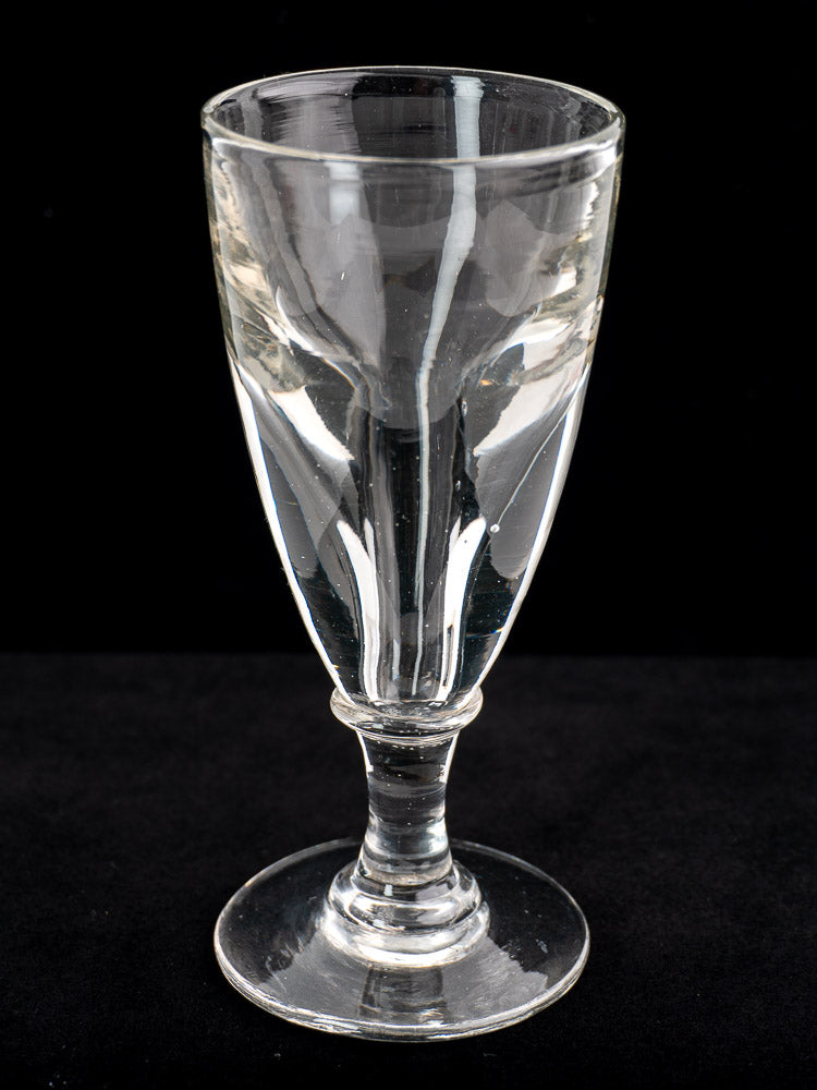 Set of four antique French uranium absinthe glasses, hand-blown with thick stems, shown on a solid black background.