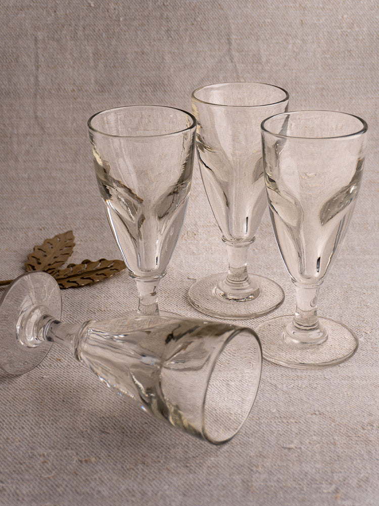 Set of four antique French uranium absinthe glasses on textured beige surface with gold leaf accent backdrop.