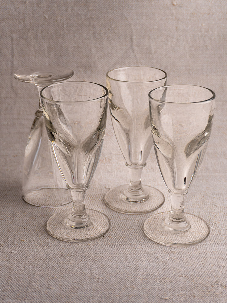 Set of four antique French hand-blown uranium absinthe glasses, three upright, one upside down on textured light fabric.