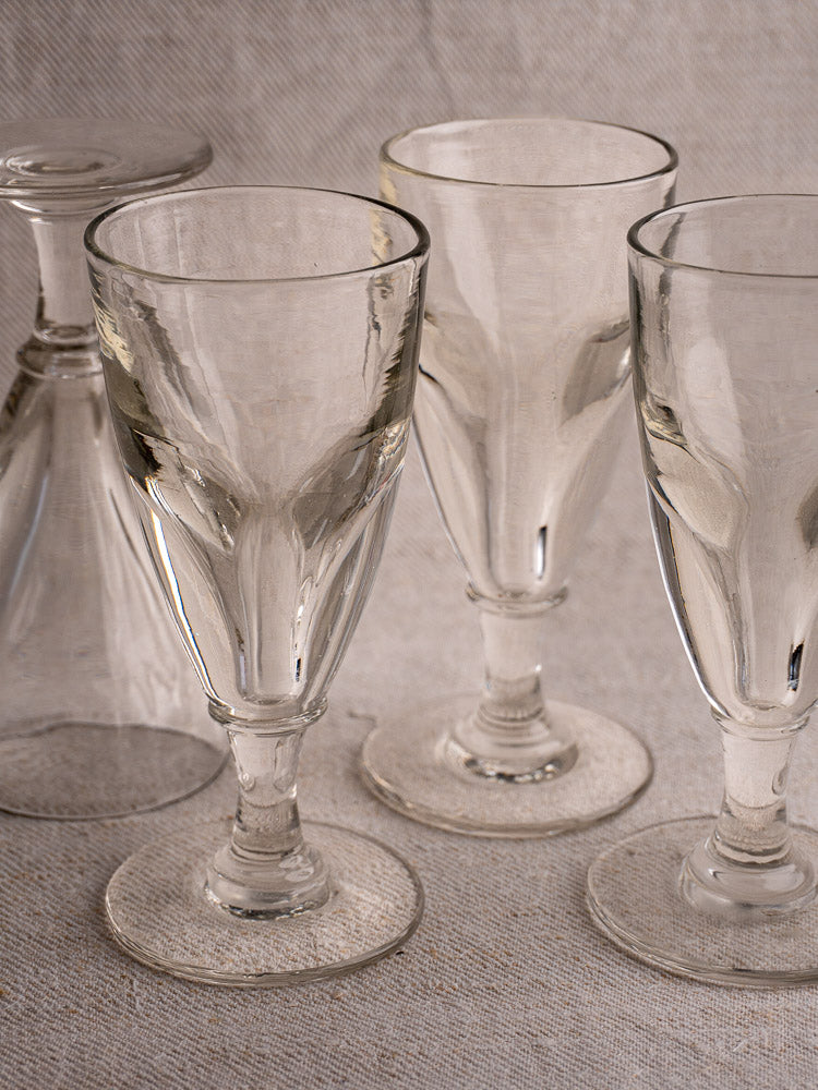 Set of four antique French uranium absinthe glasses, hand-blown, on textured surface with light fabric backdrop.