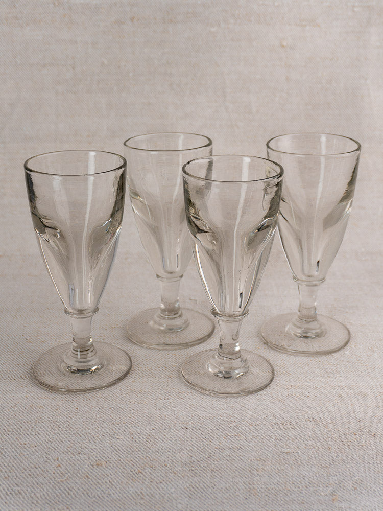 Set of four antique French uranium absinthe glasses, hand blown, grouped on light textured fabric background.