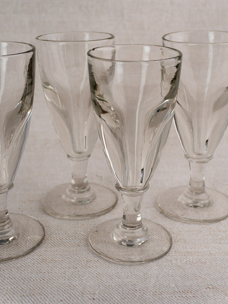 Set of four antique French uranium absinthe glasses, hand-blown with short stems and wide bases on a neutral surface.