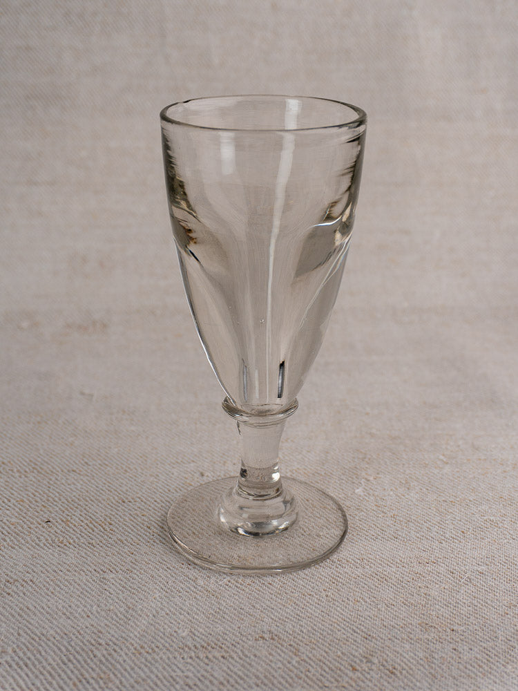 Set of four antique French uranium absinthe glasses with short stems and wide bases on textured beige surface.