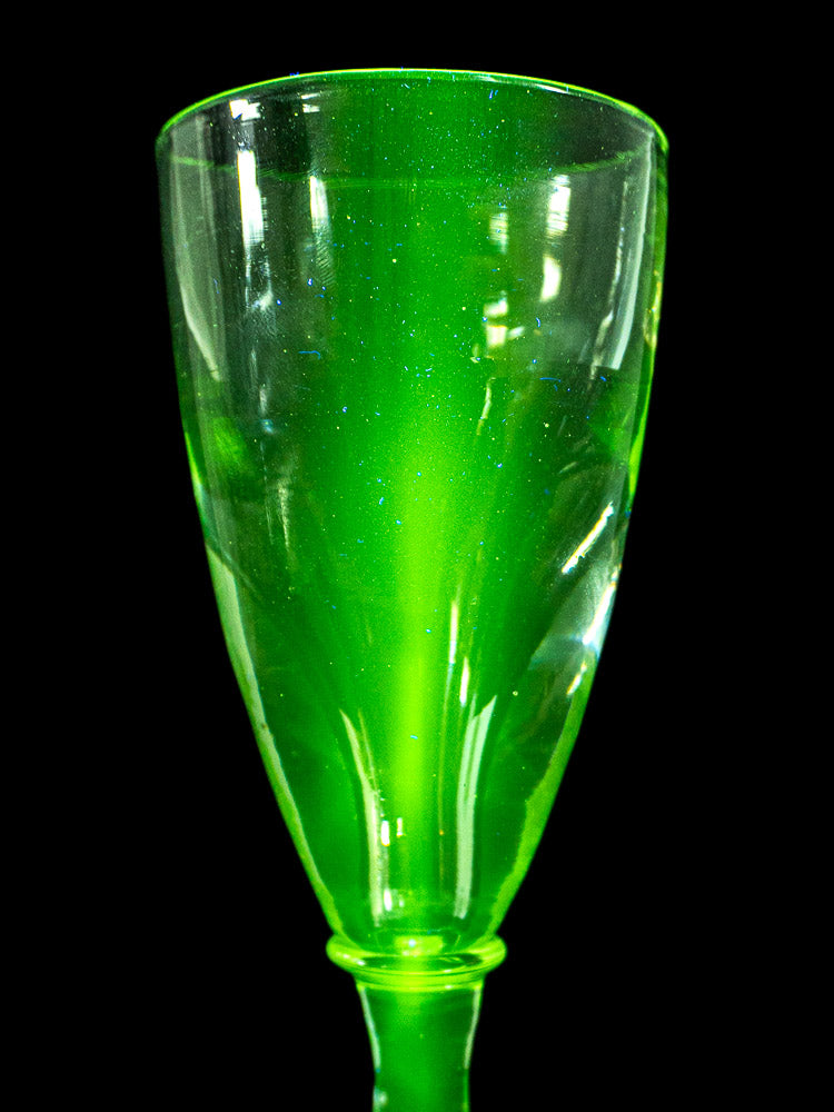 Set of 4 antique French uranium absinthe glasses glowing vivid green under UV light, black background.