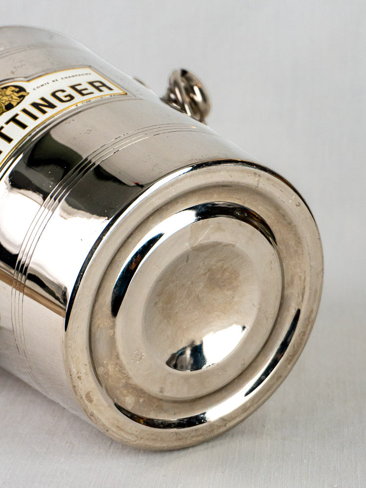 Shiny silver base of vintage Taittinger French champagne bucket with yellow and black label detail.