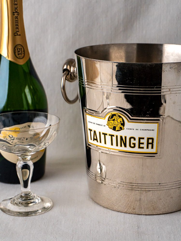 Vintage French Taittinger champagne bucket with champagne bottle and glass on light surface.