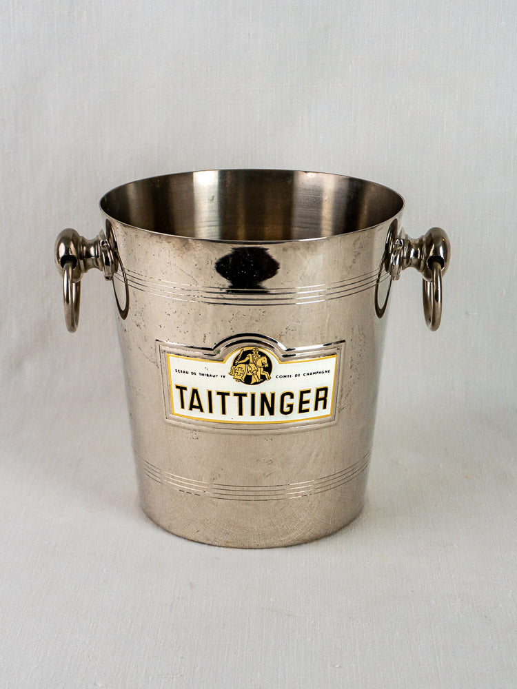 Vintage French Taittinger champagne bucket with dual metal ring handles on a light surface.