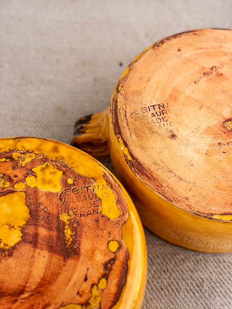 Pair of mid-century yellow-glazed French Aegitna Vallauris bowls upside down on beige fabric, showing maker's stamp.