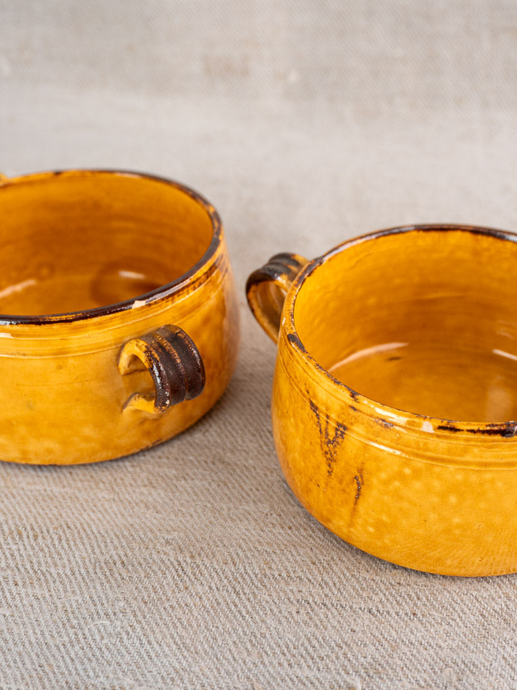 Pair of vintage French Vallauris bowls with small handles, glazed yellow-brown finish and rustic dark streaks.