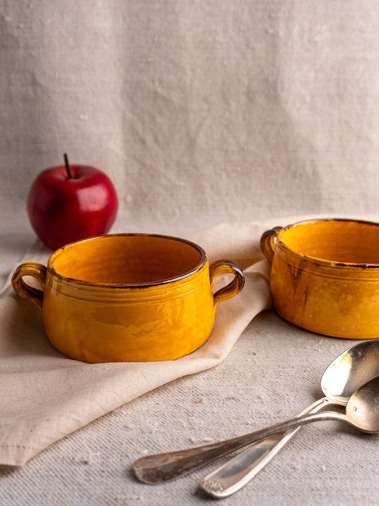 Pair of vintage French Aegitna Vallauris pottery bowls with double handles on textured beige fabric.