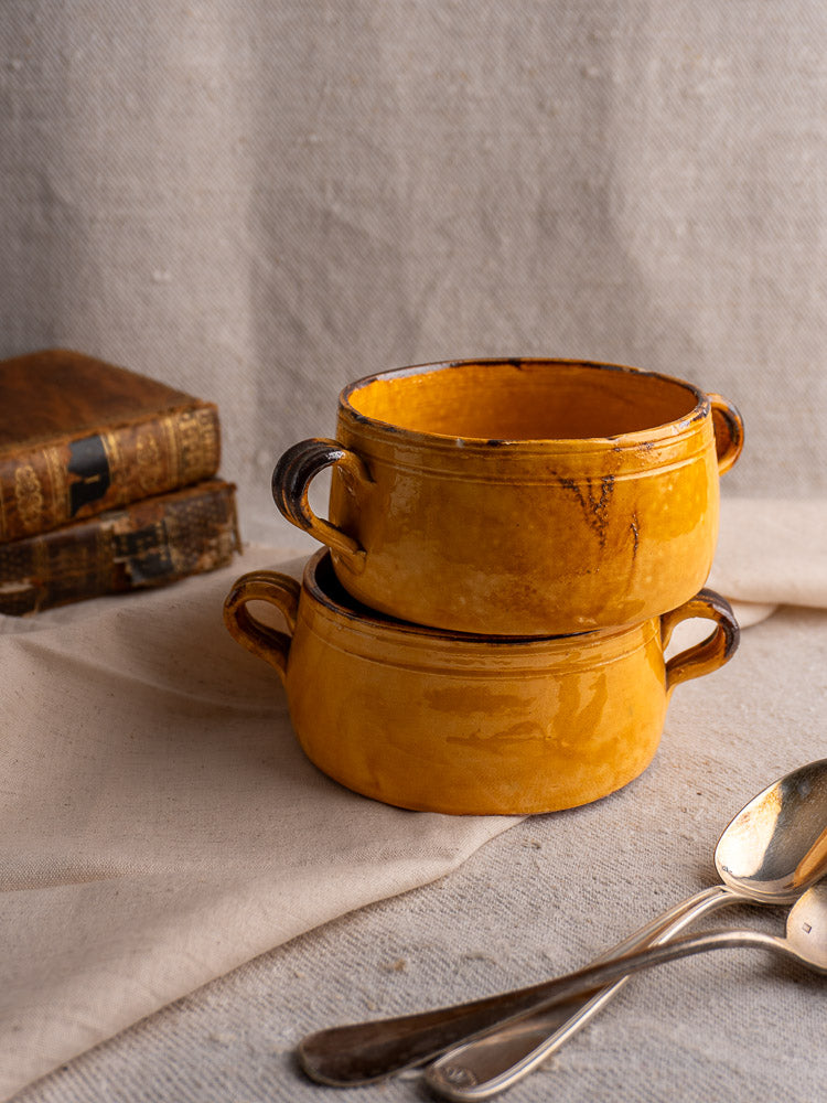 Pair of vintage French Aegitna Vallauris pottery bowls stacked on beige cloth with books and silver spoons.