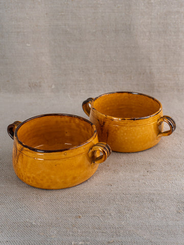 Pair of vintage French Aegitna Vallauris pottery bowls with double handles on textured beige fabric.