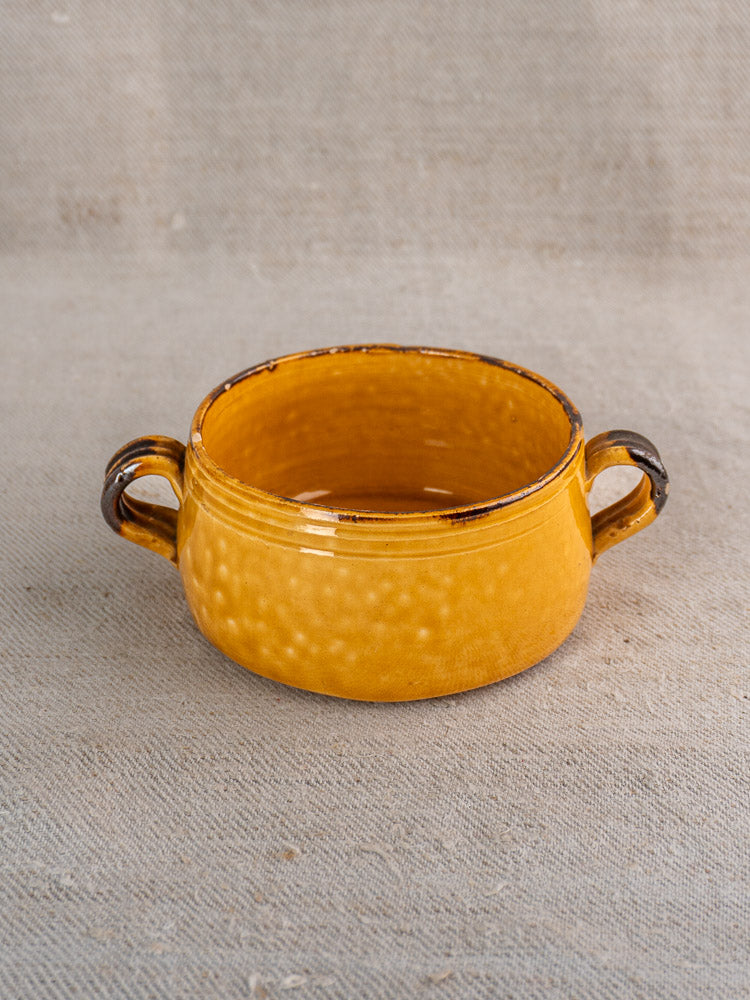Vintage French yellow Vallauris pottery bowl with two handles, glossy dimpled surface, on textured beige fabric.