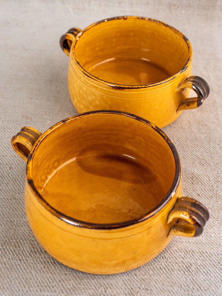 Pair of yellow French Vallauris ceramic bowls with brown rims and handles, rustic mid-century pottery craftsmanship.
