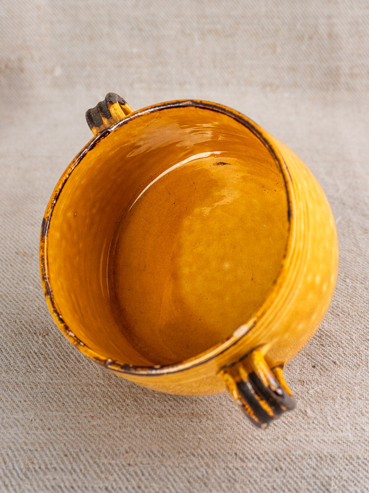 Vintage round yellow Vallauris ceramic bowl with dark handles on textured fabric, classic French mid-century pottery.
