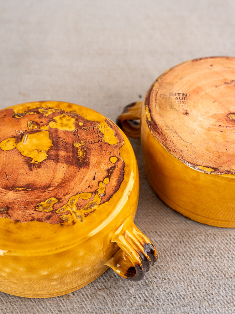 Pair of yellow vintage Aegitna Vallauris bowls upside down, maker’s marks visible on textured beige surface.