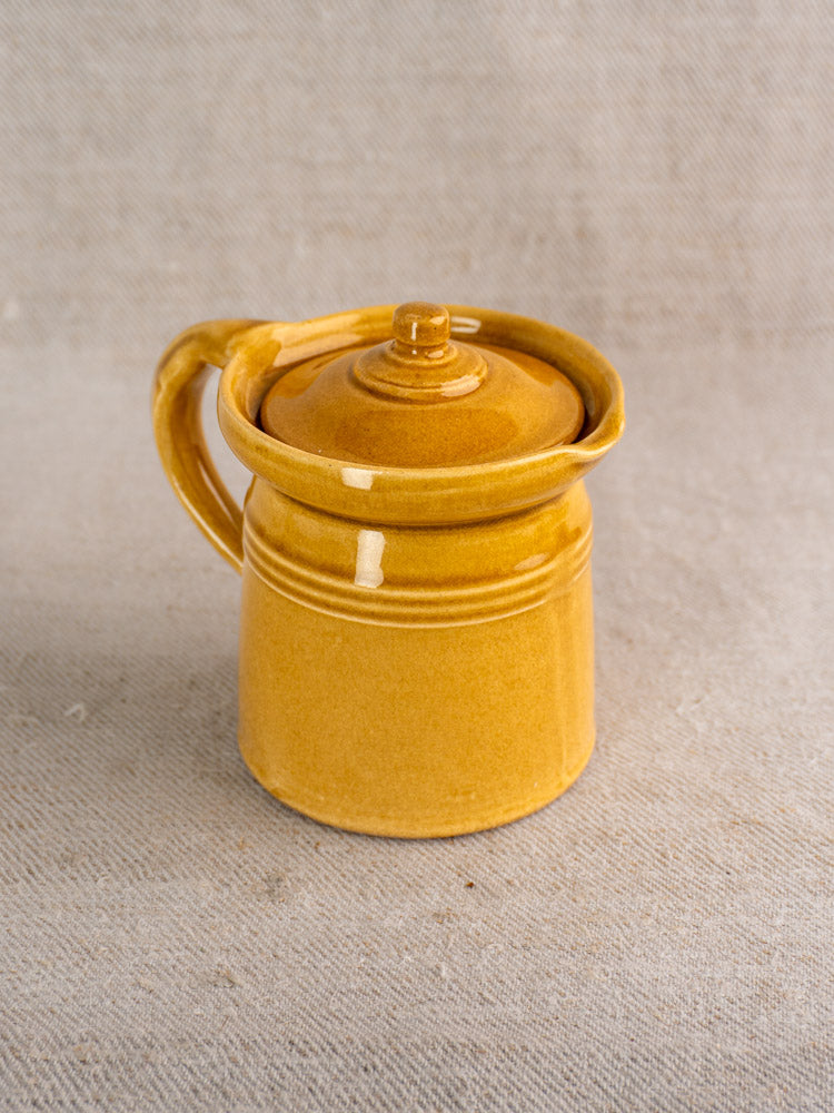 Antique French lidded pot à lait with honey ochre glaze, mid 20th century, on textured beige fabric.