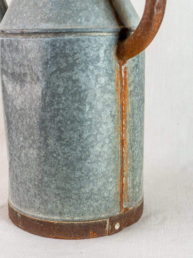 French galvanized zinc watering can with weathered gray finish and rusted handle, vintage garden decor.