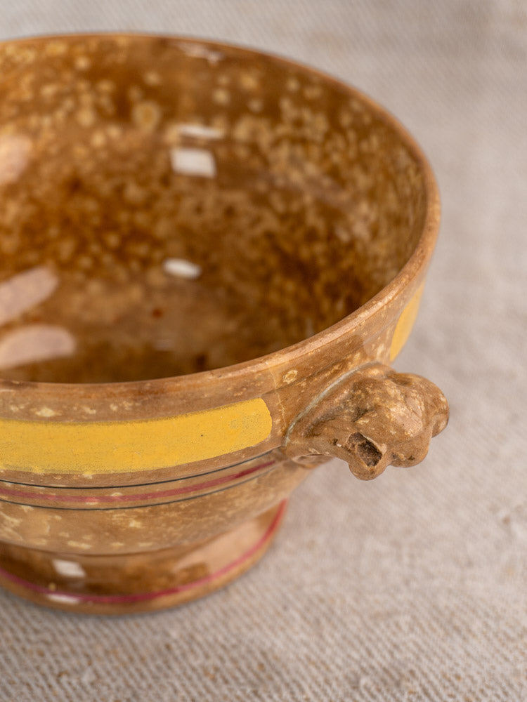 Antique French faïence bowl by HB et Cie Choisy-le-Roi with yellow stripe and animal head rim on beige fabric.