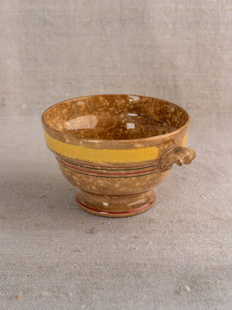 Antique French faïence bowl by HB et Cie Choisy-le-Roi with brown glaze, yellow stripe, red line, and side handle on beige fabric.