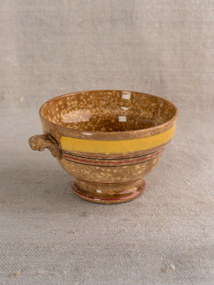 Antique French faïence bowl by HB et Cie Choisy-le-Roi with jaspé glaze, yellow rim, animal-head handle on beige fabric.