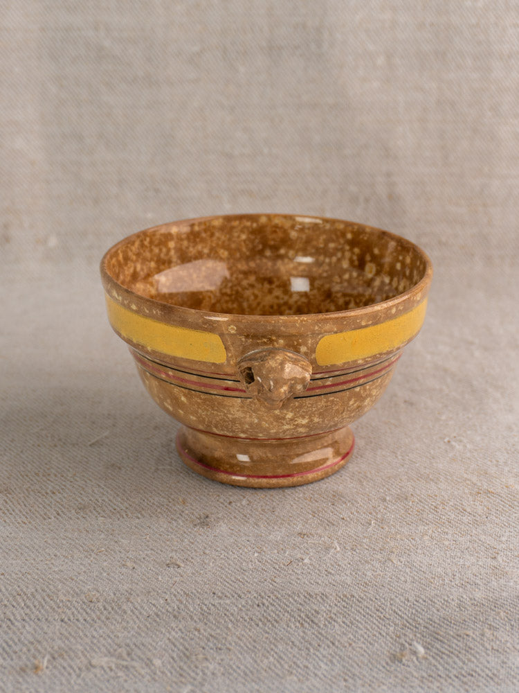 Antique French faïence bowl by HB et Cie Choisy-le-Roi with brown glaze, yellow stripe, red accents, animal handle on beige fabric.