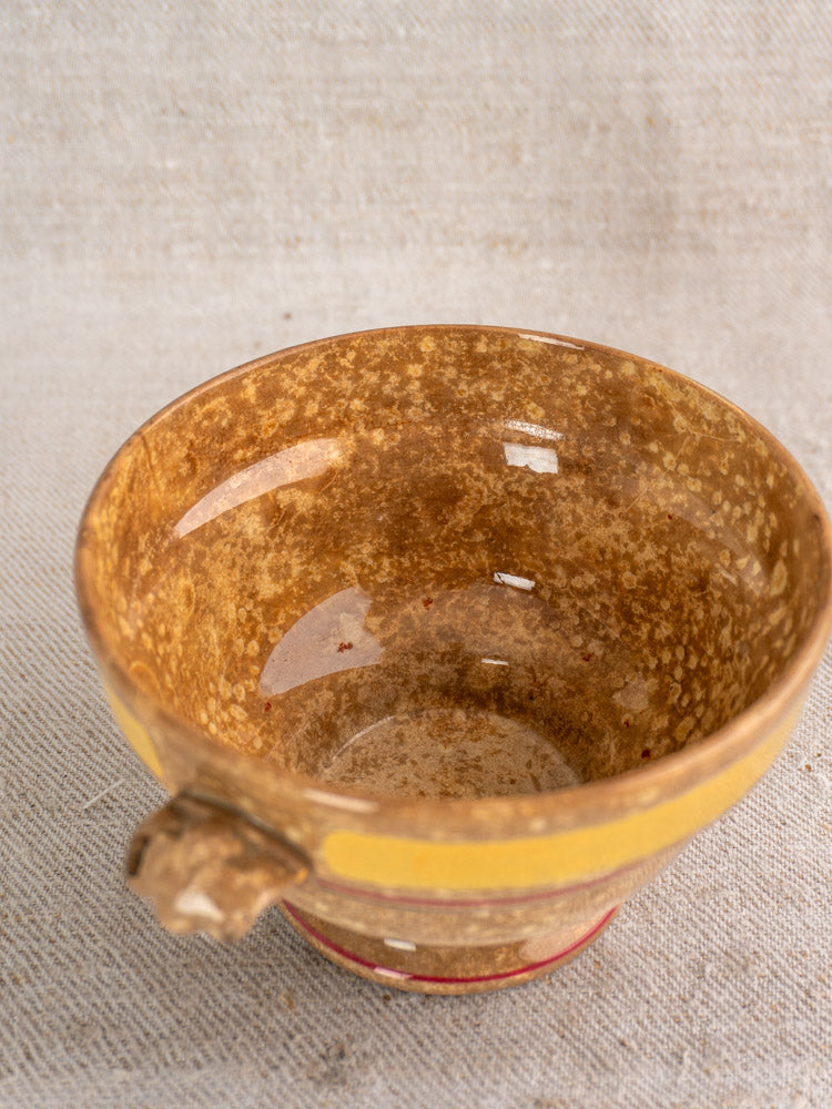 Antique French faience bowl by HB et Cie Choisy-le-Roi with brown glaze, yellow rim stripe, and small handle on beige fabric.