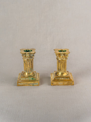 Pair of antique French gilded brass candlesticks, Louis XVI style, with column designs and square bases on light gray surface.