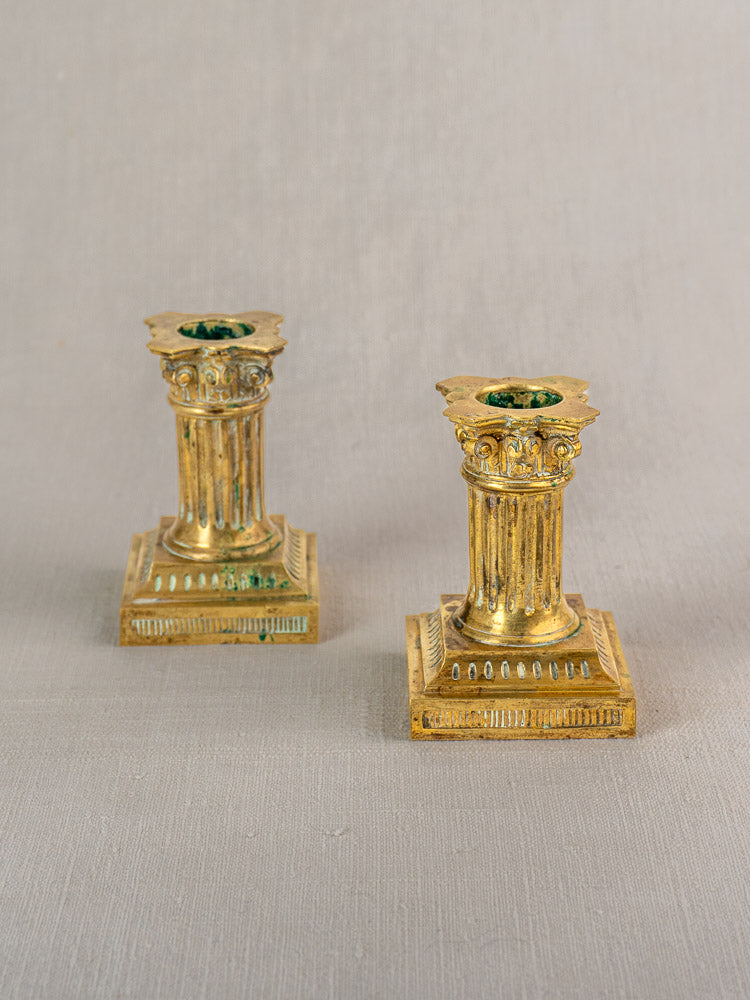 Pair of antique French Louis XVI gilded brass candlesticks with fluted columns and square bases on a light textured surface.