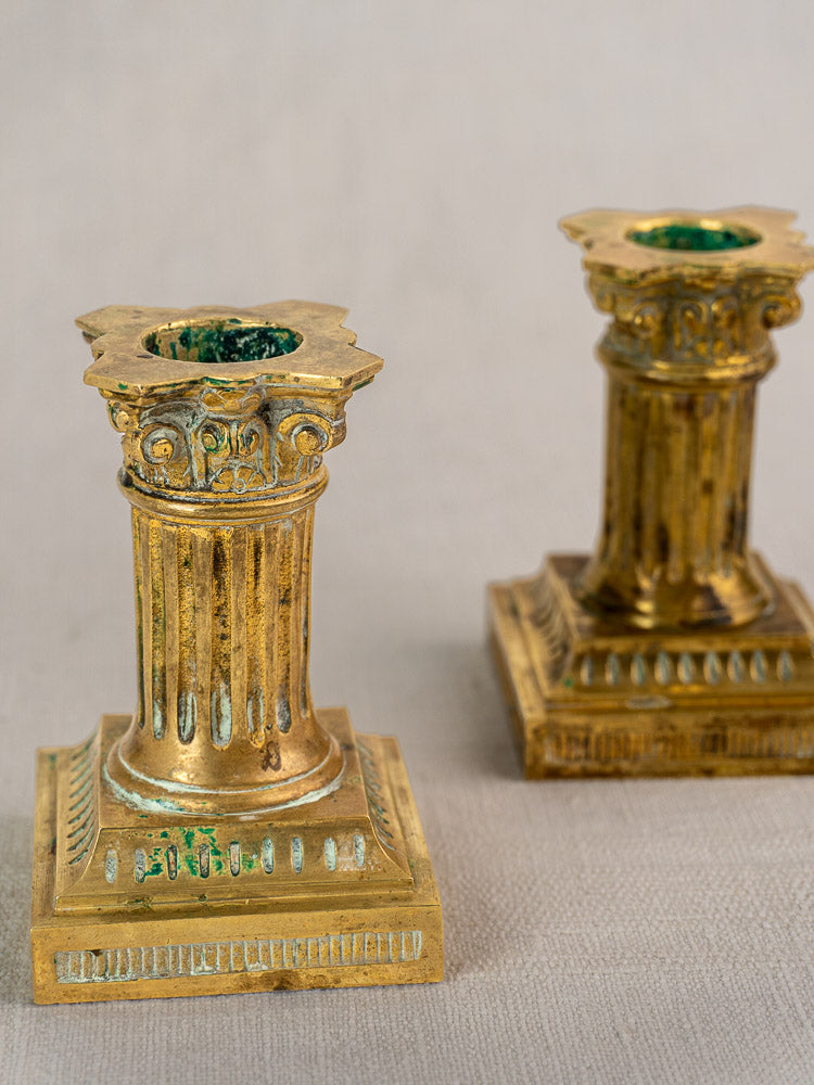 Pair of Louis XVI style antique French candlesticks in gilded brass with green accents on a textured surface.