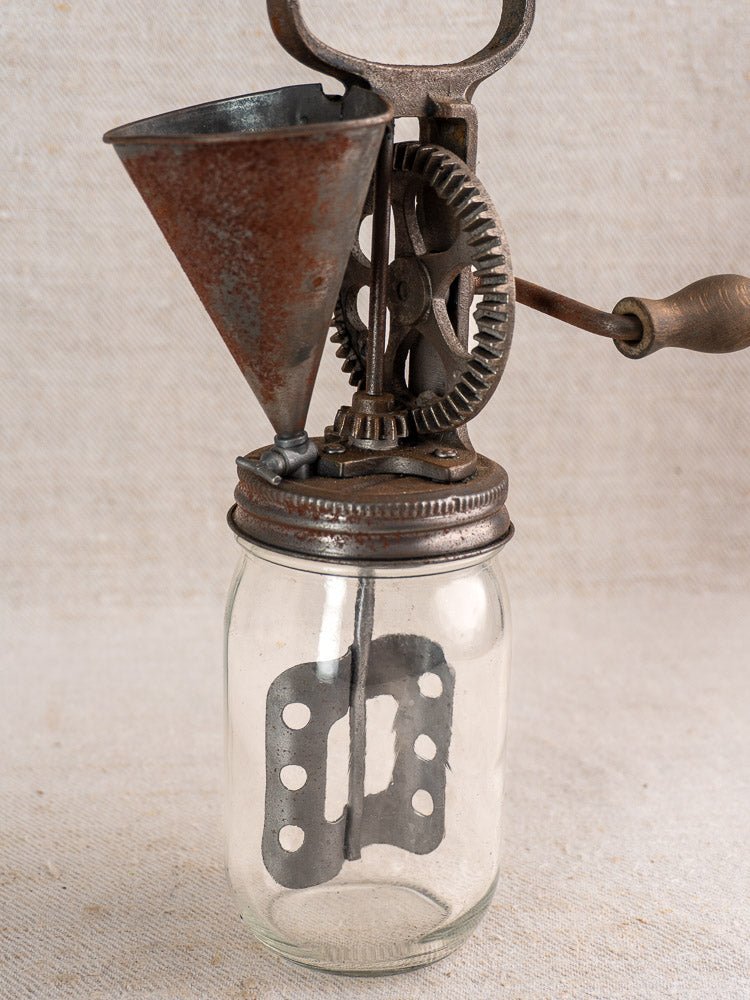 Antique French mayonnaise maker, circa 1900, with cast iron crank and glass jar on fabric background.