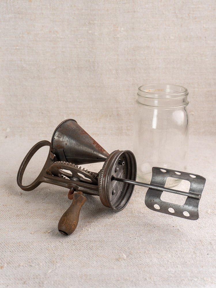Antique French mayonnaise maker with cast iron crank and wooden handle beside a glass mason jar.