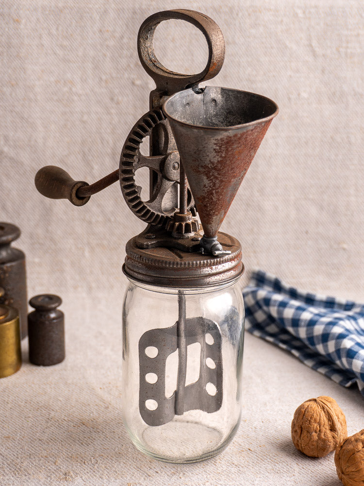 Antique French mayonnaise maker, c. 1900, with cast iron crank and glass jar, on fabric backdrop.