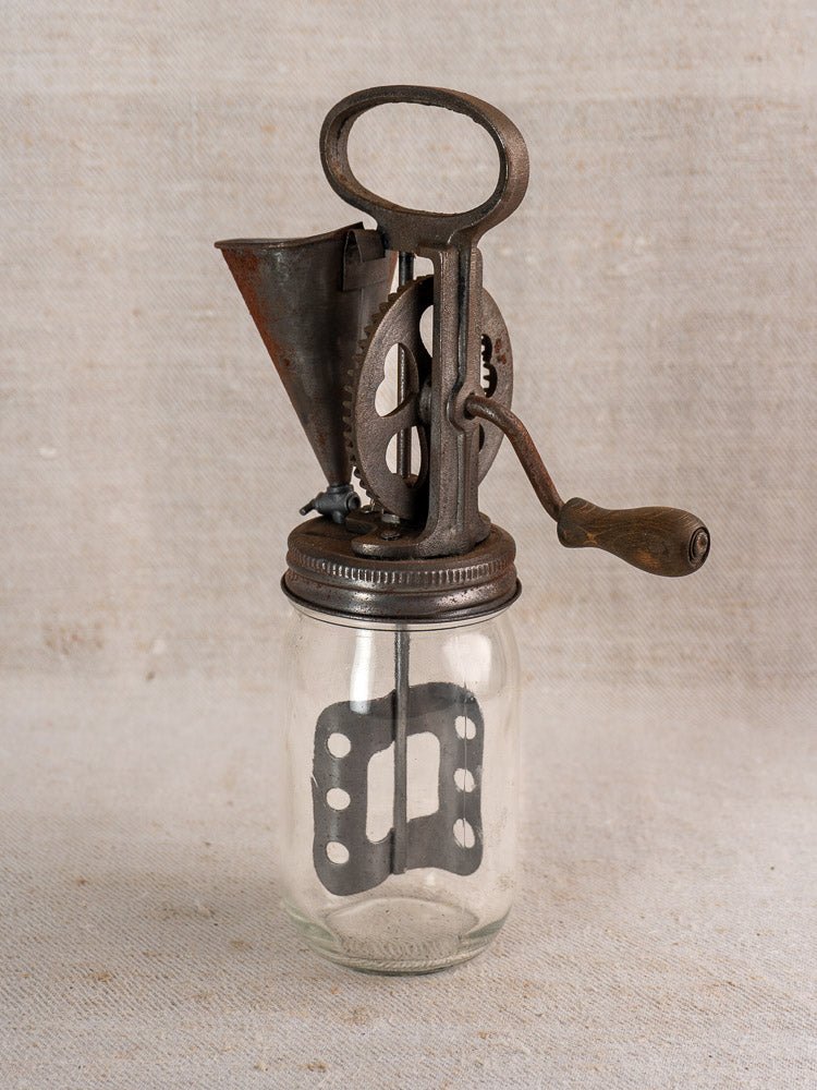 Antique French cast iron mayonnaise maker with glass jar, circa 1900, on a textured beige surface.