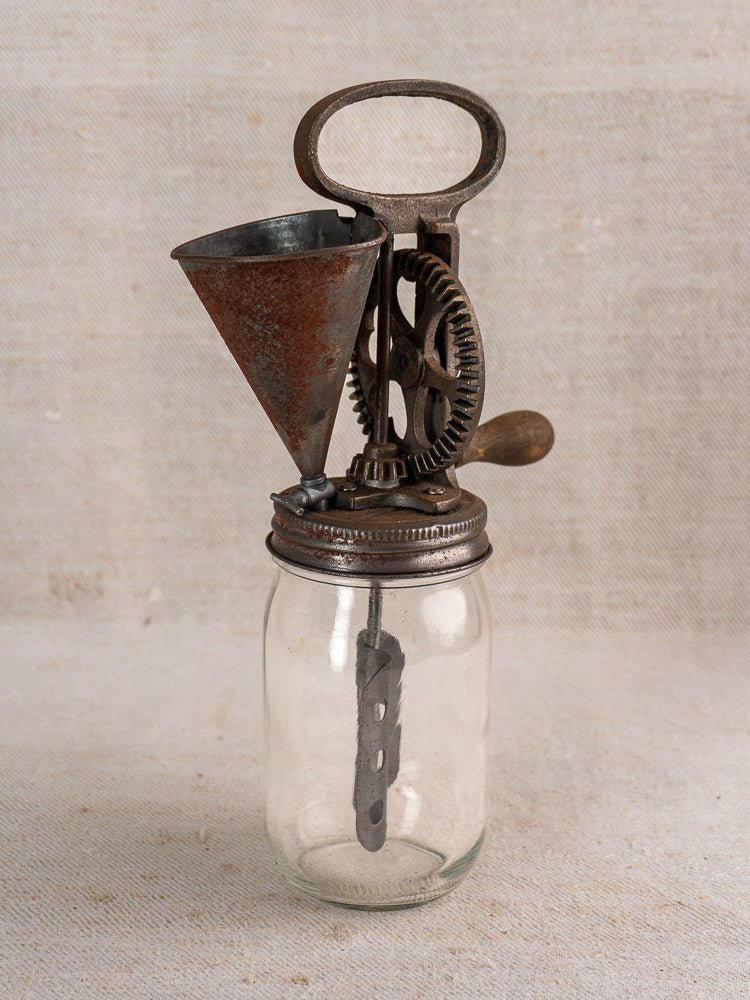 Antique French hand-cranked cast iron mayonnaise maker with gears and funnel on glass jar.