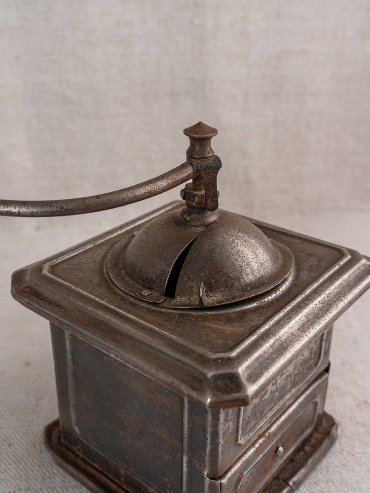 Antique French Peugeot Frères tinned steel coffee mill with domed lid and turning handle, on fabric background.