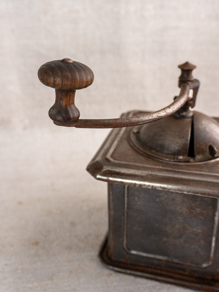 Antique French Peugeot Frères coffee mill, tinned steel with wooden handle, on neutral textured surface.