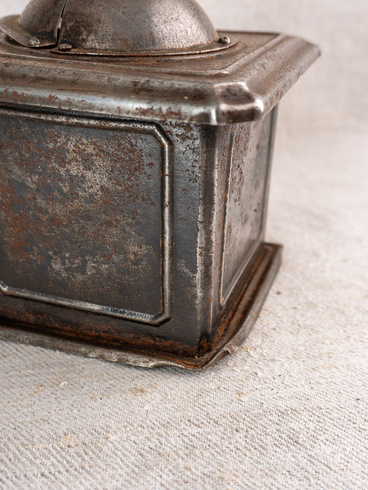 Antique French Peugeot Frères tinned steel coffee mill with aged patina on light fabric surface.