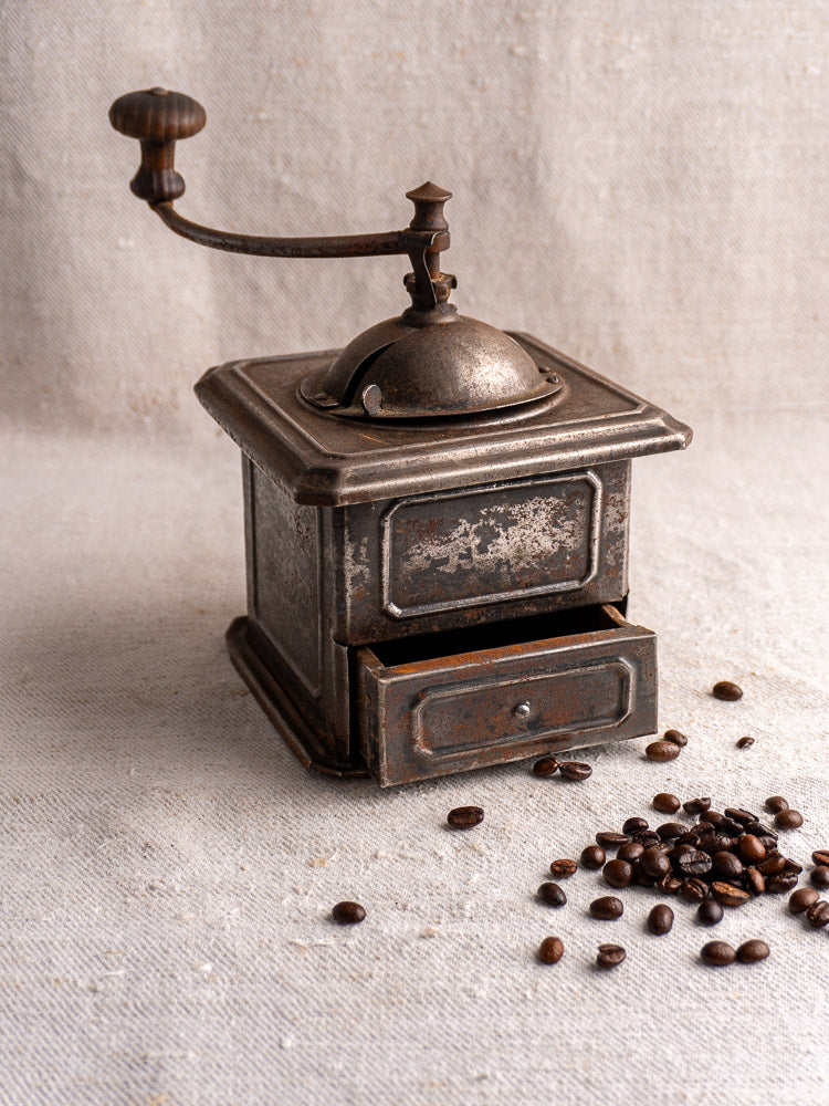 Antique French Peugeot Frères tinned steel coffee mill with hand crank and open drawer on textured surface.